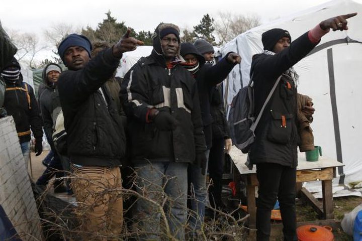 Migrants point at burning tents at the makeshift camp near Calais