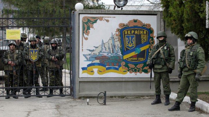 Ukrainian soldiers, left, and unidentified gunmen, right, stand at the gate of an infantry base...