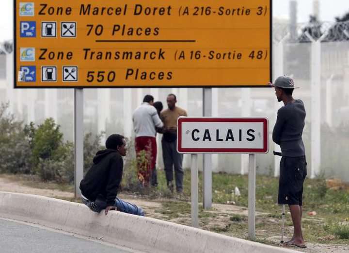 Migrants stand near a city sign along a road near the makeshift camp called ''The New Jungle'' 